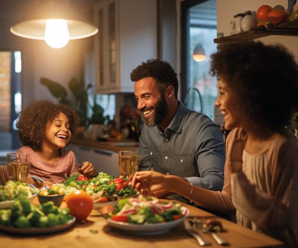 Uma família sentada à mesa durante o jantar. A mesa está cheia de pratos saudáveis e coloridos. A criança está sorrindo e pegando uma nova leguminosa com curiosidade, enquanto os pais a observam com um olhar encorajador.